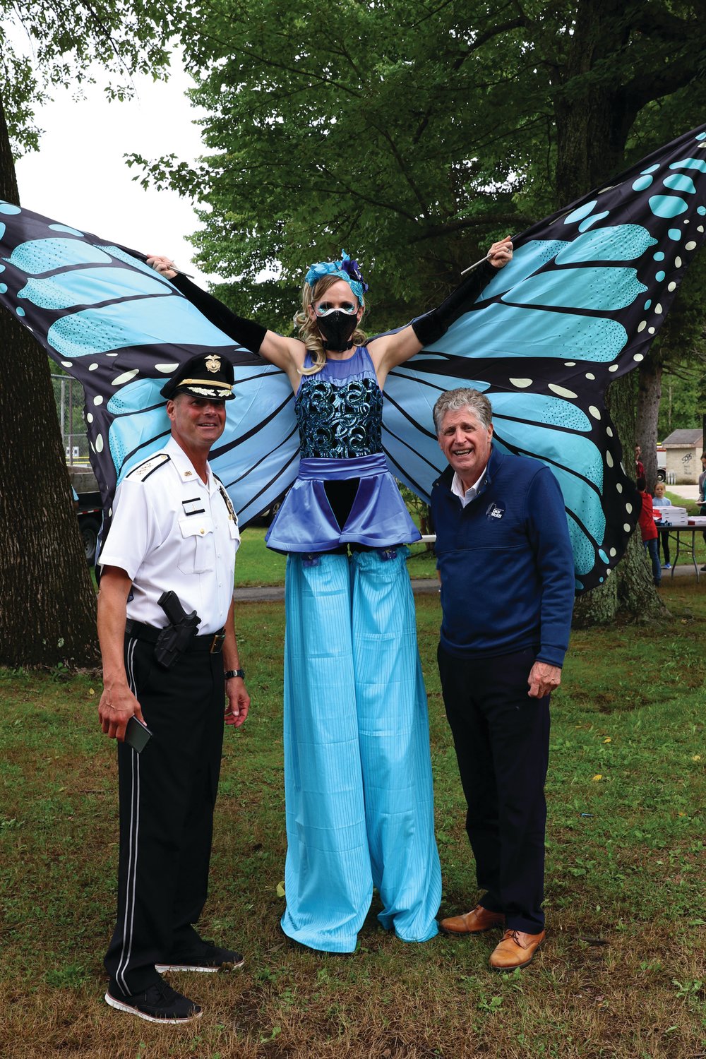 GRAND GUESTS: Gov. Daniel J. McKee and Johnston Police Chief Joseph P. Razza are joined by this beautifully dressed stilt walking butterfly that was one of many special attractions during the recent National Night Out.